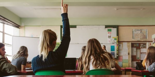 Back of a classroom with a student's hand raised.